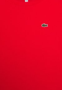 Röd bomull t-shirt med en liten grön krokodil-logotyp på bröstet. Enkel design med rund hals och en mjuk textur.