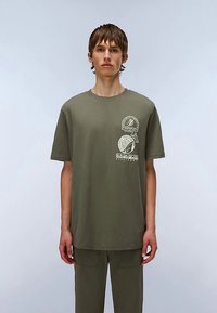 Oliwkowo zielony bawełniany t-shirt z krótkimi rękawami, okrągłym dekoltem i białym nadrukiem. Charakteryzuje się luźnym krojem i gładką fakturą.