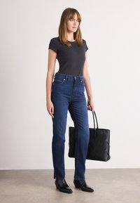 Černé krátké rukávy přiléhavé tričko, modré džíny s vysokým pasem, černá prošívaná tote bag a černé špičaté kotníkové boty. Minimalistický design.