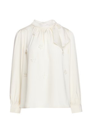 Cream long-sleeve blouse with high neckline, small floral appliques, gathered fabric near collar, and a side bow detail.