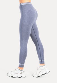 Blaue Sportleggings mit einem gerippten Bund, glatter Textur und weißen Akzentstreifen am Knöchel. Kombiniert mit weißen Sneakern.