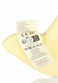 Mäkký žltý plyšový výrobok so štítkom obsahujúcim pokyny na starostlivosť a informácie o materiáloch, vrátane bavlny a polyuretánovej peny ako výplne.