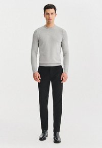 Szary sweter dzianinowy z okrągłym dekoltem, połączony z czarnymi spodniami slim-fit i czarnymi botkami za kostkę, na białym tle.