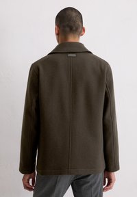 Zielono-oliwkowy wełniany płaszcz z ząbkowanym kołnierzem, usztywnionymi ramionami i prostym krojem, charakteryzujący się teksturowanym materiałem i minimalistycznymi detalami przeszyć.