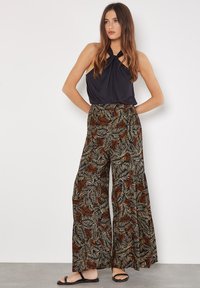 Black halter top with knot detail paired with wide-leg pants featuring a leaf pattern in red, beige, and black. Sandals complete the outfit.
