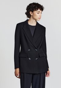 Blazer nero doppiopetto con revers, vestibilità sartoriale e due tasche frontali. Presenta bottoni lucidi e una texture del tessuto liscia.