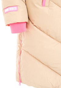 Beige Puffer-Jacke mit rosa Akzenten, ausgestattet mit einem "GOOD VIBES"-Aufnäher, gerippten rosa Bündchen und einem rosa Reißverschluss. Chevron-gequiltetes Design.