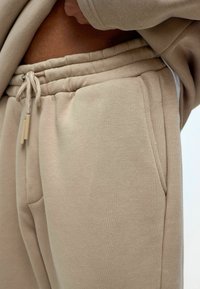 Beige joggings gemaakt van een zachte katoenen mix, met een elastische tailleband met een trekkoord en zijzakken. Textuurafwerking.