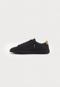 Black low-top sneaker with lace-up front, side zipper, and tan heel tab on plain white background.