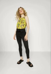 Top de tanque amarelo com padrões florais, calças pretas de cintura alta com laço e sandálias pretas de slip-on. Texturas suaves e design ajustado.