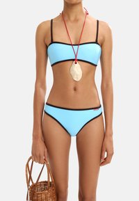 Niebieski zestaw bikini z czarnym wykończeniem; top bandeau i majtki o średnim stanie. W zestawie duży kremowy wisiorek na czerwonym sznurku oraz pleciona torba.