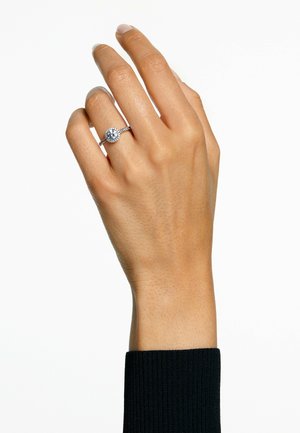 Anello di fidanzamento in argento con una pietra centrale rotonda circondata da pietre più piccole, impostato su una fascia sottile, indossato su una mano con una texture della pelle naturale.