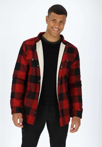 Röd och svart rutmönstrad flanellskjorta med ett vitt fleecefoder, med knäppning framtill och långa ärmar. Svart T-shirt och byxor bärs under.
