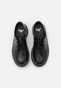 Černé kožené šněrovací boty s texturovaným povrchem, žlutým prošitím a silnou gumovou podrážkou, s logem Dr. Martens na stélce.