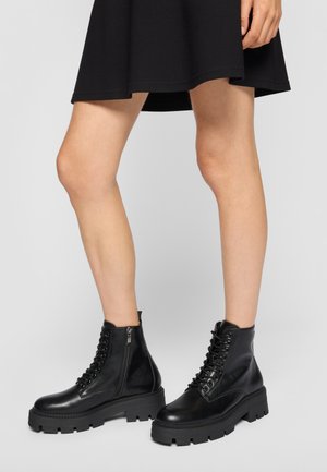 Bottines en cuir noir avec un bout arrondi, des semelles texturées, un laçage à l'avant et une fermeture éclair sur le côté pour un enfilage plus facile.