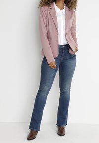 Blazer rosa chiaro con rever, due bottoni e tasche frontali; abbinato a una camicia bianca e jeans svasati blu scuro; stivaletti marroni a caviglia.