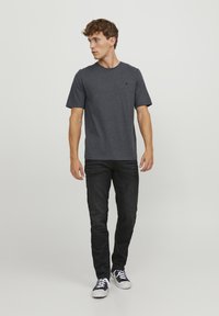 Grå kortærmet t-shirt i blødt stof, parret med sorte jeans og sort-hvide sneakers. Enkel design med rund halsudskæring.