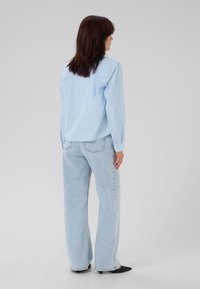 Camicia button-up azzurro chiaro a maniche lunghe abbinata a jeans in denim chiaro a vita alta e gamba larga, con scarpe nere a punta.
