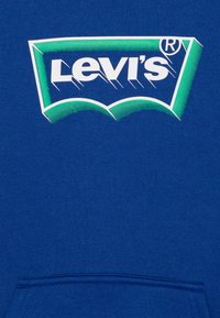 Sweatshirt bleu arborant un grand logo Levi's blanc et vert avec un design incurvé. Le tissu est lisse ; comprend une poche avant.