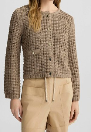 Femme portant un cardigan en maille texturée taupe avec des boutons ronds, associé à un short beige taille haute avec poches plaquées devant et cordon de serrage.