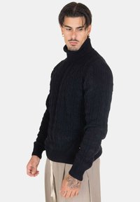 Maglione realizzato in nero con lavorazione a trecce, colletto alto, polsini e orlo a costine, caratterizzato da un motivo testurizzato e una silhouette aderente.