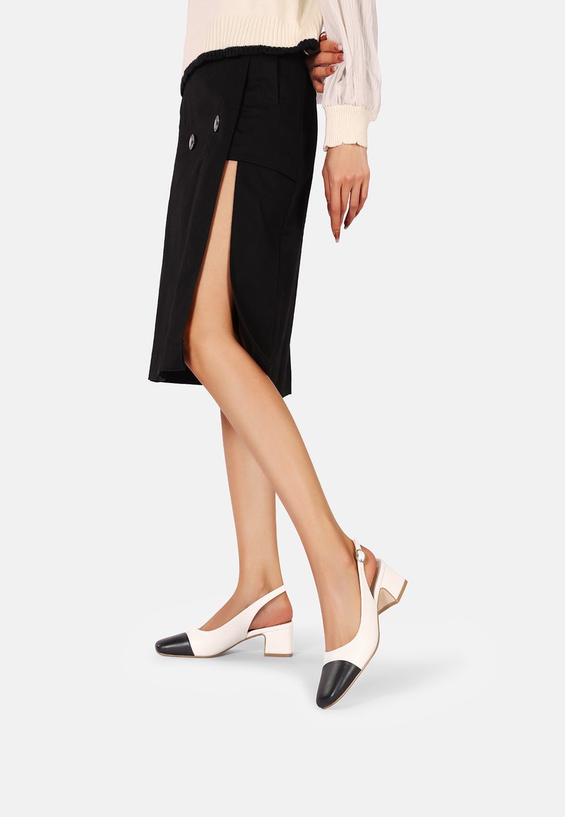 Tacchi slingback bicolore bianco e nero con tacco a blocco, caratterizzati da una punta arrotondata e una fibbia laterale. Texture in pelle liscia.