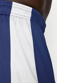 Shorts sportivi blu navy con strisce laterali bianche, realizzati in un tessuto texturizzato e con un elastico in vita. Vista ravvicinata che mette in evidenza il contrasto di colore.