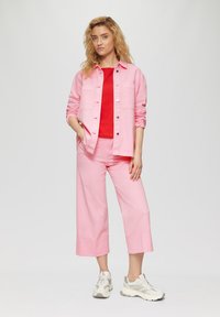 Veste en denim rose et pantalon large avec un haut en maille rouge. L'ensemble a une coupe décontractée et est associé à des baskets beiges.