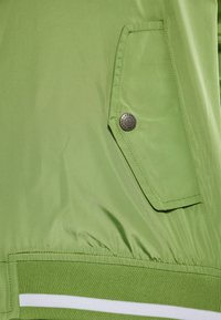 Giacca a vento verde con orlo a coste e accenti a righe. Progettata con un tessuto testurizzato e un dettaglio con tasca a scatto.