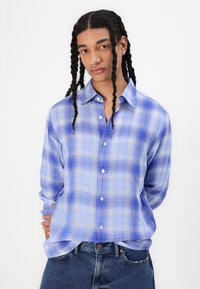 Blue plaid button-up shirt with a relaxed fit, long sleeves, and soft texture. Features light and dark blue tones with white accents.