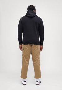 Sudadera con capucha negra, combinada con pantalones cargo color caqui con bolsillos laterales, y zapatillas blancas con rayas negras.
