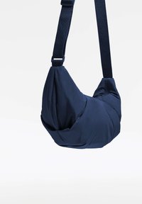 Sac à épaule bleu marine au design rond et structuré. Fabriqué en tissu doux et texturé avec une bandoulière réglable et des coutures distinctives.