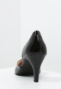 Chaussure à talon haut en cuir verni noir avec un bout pointu, un talon fin et un dos incurvé. Texture lisse avec peu d'ornements.