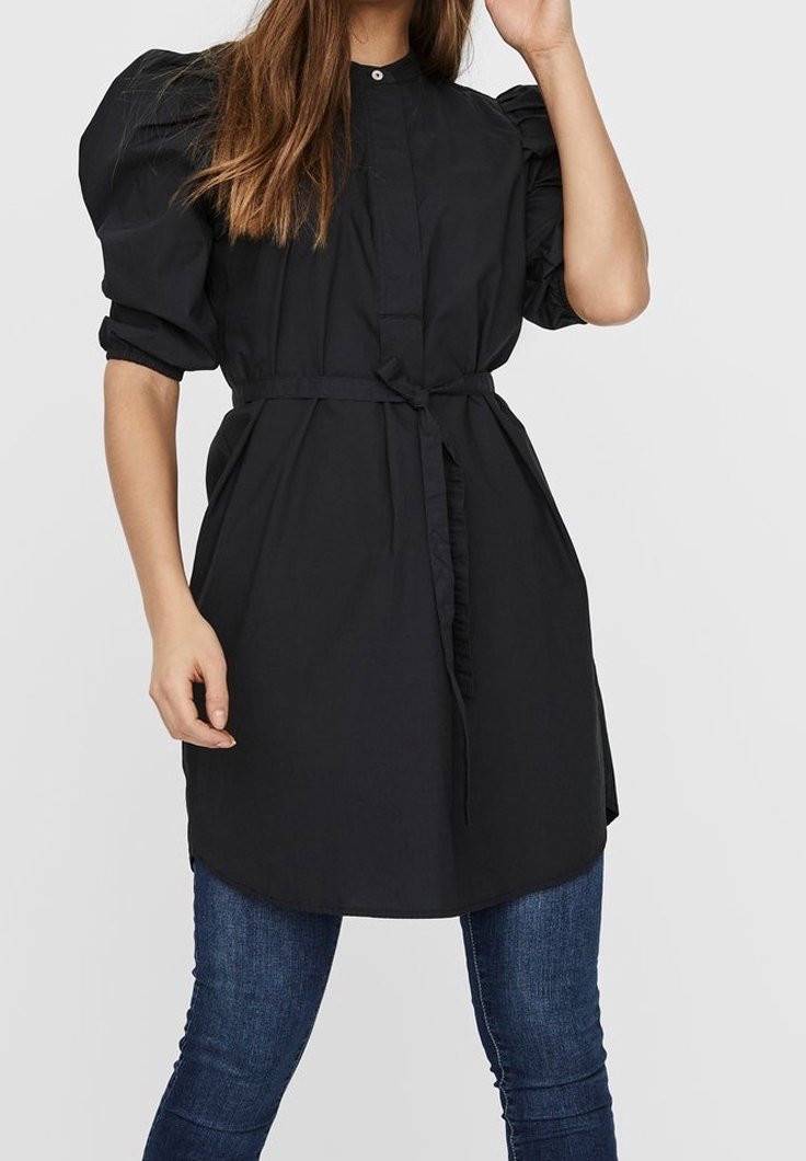 Schwarzes, übergroßes Hemdkleid aus Baumwolle mit Puffärmel, Knopfverschluss vorne und Taillengürtel, kombiniert mit schmalen Jeans.