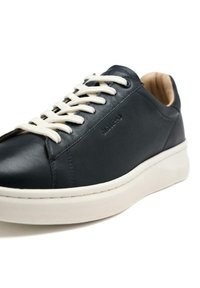 Zapatilla de cuero navy con cordones blancos, puntera redonda y forro beige. Cuenta con una suela blanca plana y un logotipo en relieve en el lateral.
