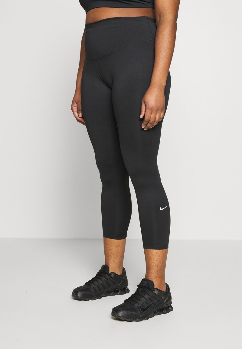 Black, high-waisted leggings with a textured finish, cropped to mid-calf. Features small white Nike logo near the calf. Worn with black sneakers.