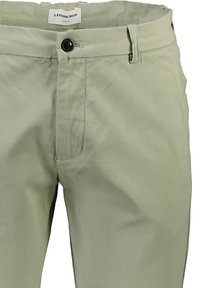 Pantalons ajustés en tissu vert clair avec une texture lisse. Dotés d'une fermeture à bouton, d'un zip et de poches avant.