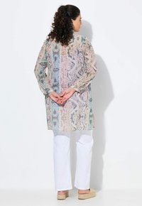 Tunic lunga e stampata in colori pastello con una texture semi-trasparente, dotata di maniche lunghe e un taglio dritto, abbinata a pantaloni bianchi.