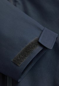 Tejido azul marino con una textura suave, que presenta un cierre de velcro en el puño y detalles de costura precisos a lo largo de los bordes.