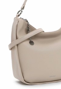 Borsa a tracolla in pelle beige con texture, con una cinghia sottile, cerniera argentata e ciondolo metallico circolare con il marchio "SURI FREY".