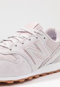 Hellgraue Wildledersneaker mit rosa Akzenten, Gummiaußensohle, Schnürverschluß und einem auffälligen "N"-Logo an der Seite.