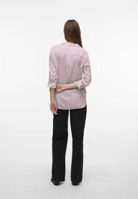 Camisa de botones a rayas rojas y blancas con mangas dobladas; combinada con pantalones negros, que presentan un corte relajado y un detalle de pliegue en la parte posterior.