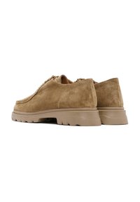 Calzado de ante en tono tostado con forma redondeada, detalles de costura y suela de goma texturizada. Los zapatos cuentan con ojales para cordones y un perfil bajo.