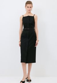 Schwarzes ärmelloses Kleid mit gerader Silhouette, dünnen Trägern, tailliertem Bund und seitlichen Taschen. Glatter Stoff und knielanges Design.
