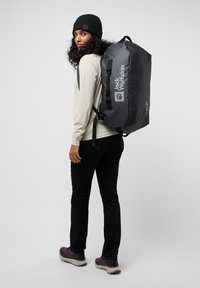 Bolsa de deporte negra con el logo de Jack Wolfskin, fabricada con material duradero, con correas ajustables, una asa superior y una forma rectangular y elegante.