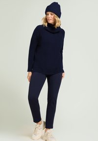 Marineblauwe gebreide trui met een colhals, geribbelde manchetten en zoom; gecombineerd met bijpassende marineblauwe broek en lichtgekleurde sneakers.