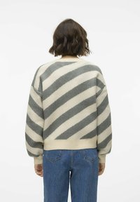 Crème kleurige trui met grijze diagonale strepen, overgrote ontwerp, geribbelde manchetten en zoom, gecombineerd met lichtblauwe denim jeans.