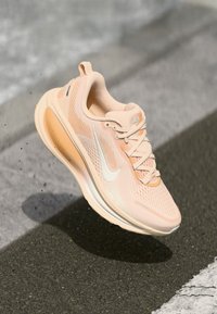 Baskets de course rose clair avec une tige en mesh respirant, accents blancs et semelle rembourrée, présentant un motif texturé et des lacets.