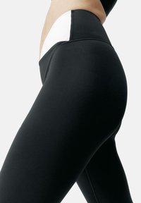 Svarta leggings med hög midja som har en kontrasterande vit panel. Slät textur, åtsittande design som framhäver kurvor och platta sömmar.