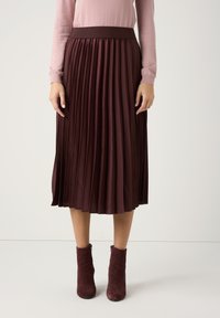 Burgundrote, plissierte Rock mit einem gerippten elastischen Bund, aus glattem Stoff, kombiniert mit burgundroten Knöchelstiefeln.